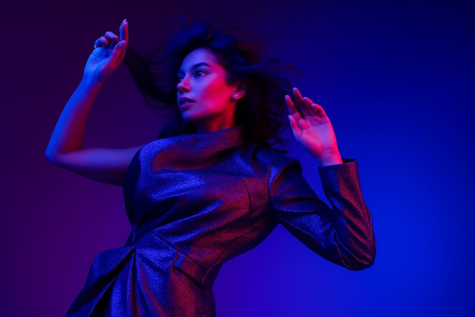 A fashion model in a metallic coat, hair caught in motion, lit in pink and blue