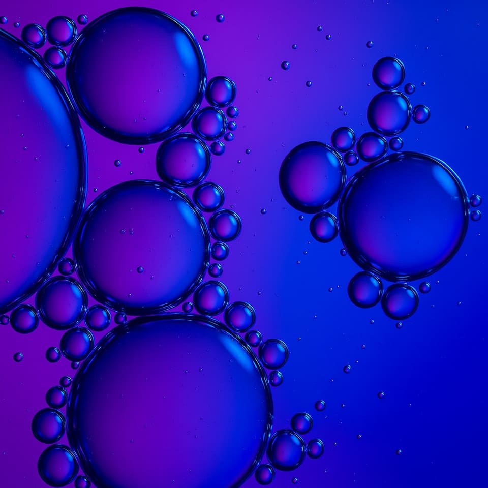 A macro photograph of liquid droplets pooling in purple and blue