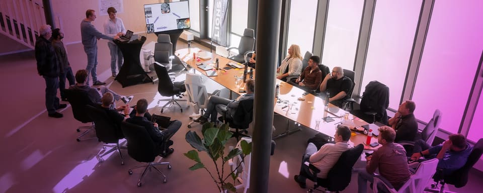 A Lionsville team session seen from above: colleagues around a long meeting table watching a presentation on a screen